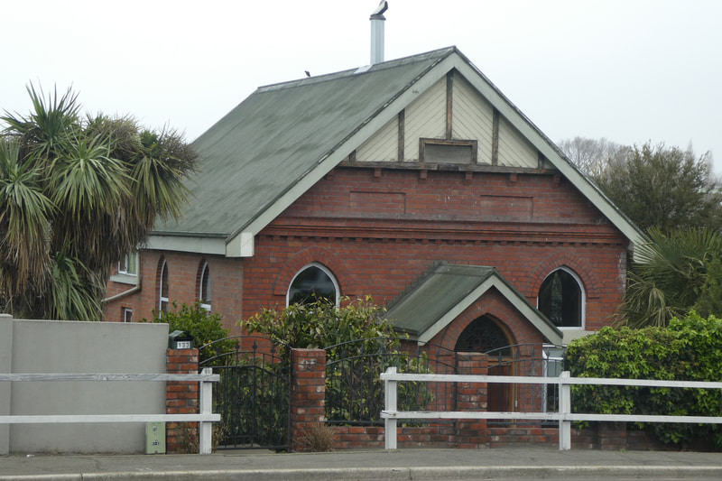 When I first came to Timaru I recall being fascinated by the charming little brick building along Evans St, in Waimataitai, and wondering about its origins.  
All Saints began its existence when it was built as a Primitive Methodist church on the Evans Street site in Waimataitai.   The Herald reported at the time that the first services were held in 1906 even though the little church wasn’t finished until the following year, 1907.
 It was to house a congregation of around 100 people and cost around 400 Pounds to complete. Constructed of red brick, on a foundation of concrete running from the road level in the front to a depth of about 6 feet at the back, in appearance it was and still is a very compact and neat building. 
The entrance is by a square porch, facing the Main North road, still visible today, above the porch is a small belfry, no longer there.  
The Herald then also reported that “the interior was covered with a ‘dead rose tint’ and the wainscoting, or wooden lining, ran to a height of 4 feet around the walls. The church is lit by Gothic headed windows, filled with tinted glass, and these give the interior a nice bright appearance. For evening services two large kerosene lamps are suspended from the ceiling”. 
In 1879 Mrs Woollcombe started a Sunday school for 11 children in her dining room at Ashbury (the site at Ashbury Park is still home to the magnificent trees planted on this estate).  A couple of relocations saw the Sunday school moved first to the Waimataitai State School and then in 1907 to a small wooden church on the Woollcombe property, the first Anglican church to the north of the city.  Every other Sunday church services were held here, and the congregation grew until a new home was needed.  In 1924 the little brick Methodist chapel in Evans Street was bought for the purpose at a cost of 455 pounds, and a new Sunday School was added on behind. 
Well supported over the years by its congregation, the church continued to operate till 1978 when All Saints and St Philip’s made the decision to combine. The Evans Street Chapel was deconsecrated and sold with proceeds set aside for the construction a new chapel at St Philips to rehouse precious items from All Saints like the St Mary’s font and the carvings by Frederick Gurnsey as well as other treasures.
The little building I used to wonder about was original brick chapel building. It still stands, having been redesigned as a private home.
The original All Saints, the small wooden church on the Woollcombe property, Ashbury, was also altered to become a family home.
